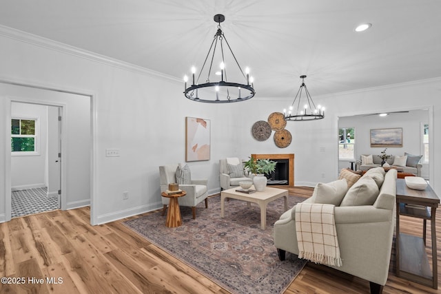 living room with a chandelier, ornamental molding, light wood-style flooring, a glass covered fireplace, and baseboards