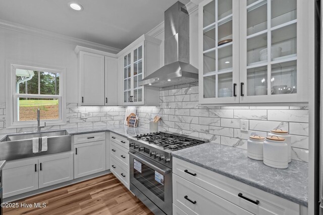 kitchen featuring high end stove, a sink, wall chimney exhaust hood, ornamental molding, and tasteful backsplash