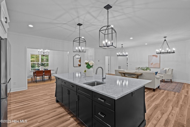 kitchen featuring a sink, a chandelier, dark cabinets, freestanding refrigerator, and light wood-style floors