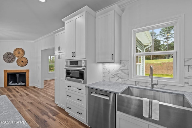 kitchen with stainless steel appliances, crown molding, a sink, decorative backsplash, and wood finished floors