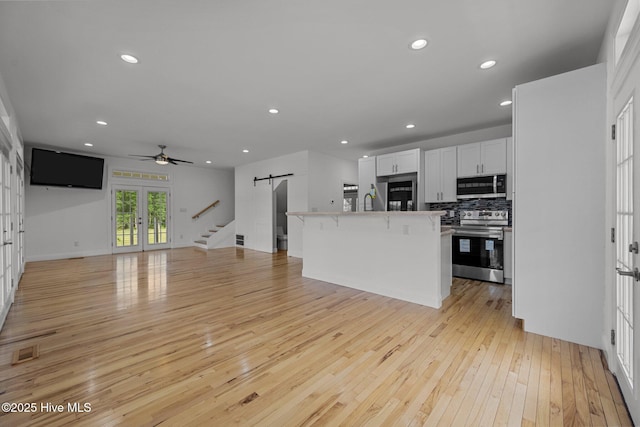 2142 Raccoon Rd, Willard, NC 28478 - kitchen featuring appliances with stainless steel finishes, a barn door, open floor plan, light wood-style flooring, and decorative backsplash