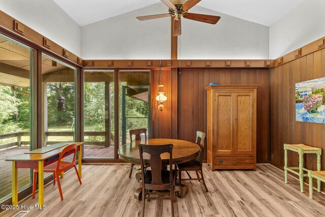 dining area featuring high vaulted ceiling, a ceiling fan, light wood-style flooring, and wooden walls