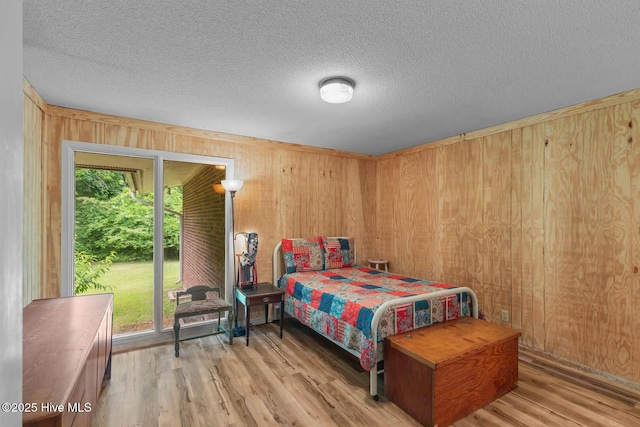bedroom featuring multiple windows, wood walls, wood finished floors, and a textured ceiling