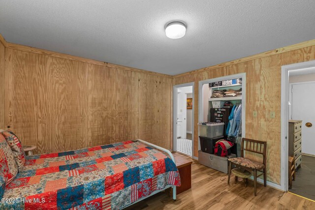 bedroom with wood walls, a textured ceiling, and wood finished floors