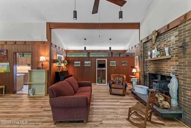 living area with wood finished floors, a wood stove, ceiling fan, wood walls, and vaulted ceiling