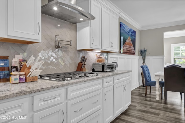 kitchen with wall chimney range hood, stainless steel gas stovetop, white cabinets, crown molding, and tasteful backsplash