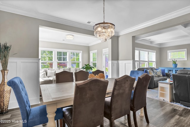 dining space with dark wood finished floors, a decorative wall, crown molding, a chandelier, and wainscoting