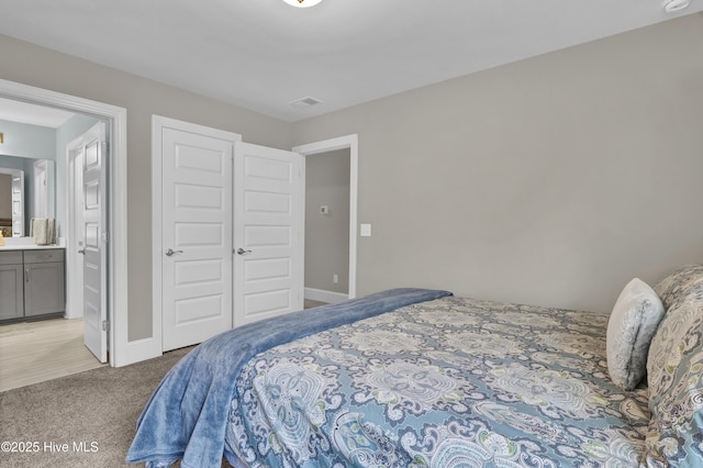 bedroom featuring light colored carpet, ensuite bathroom, and baseboards