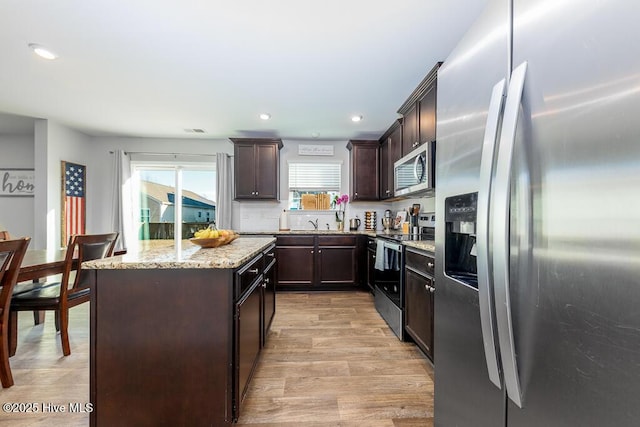 308 Isabelle St Lot # 986, New Bern, NC 28560 - kitchen featuring appliances with stainless steel finishes, light wood-style floors, dark brown cabinets, a kitchen island, and light stone countertops