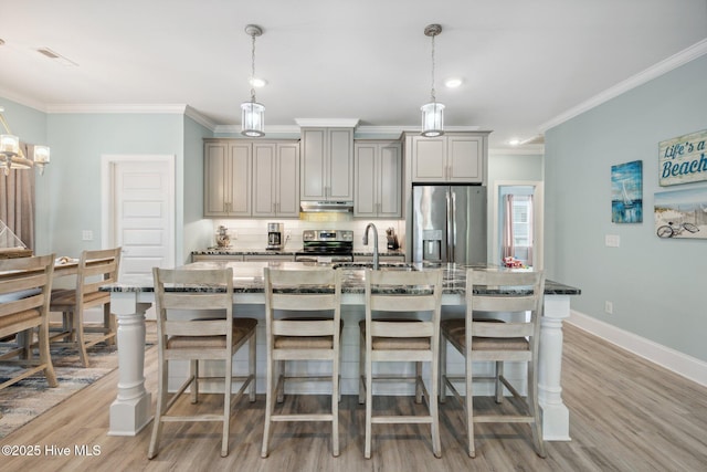 152 NW 1st St, Oak Island, NC 28465 - kitchen featuring stainless steel appliances, under cabinet range hood, crown molding, dark stone countertops, and a kitchen breakfast bar