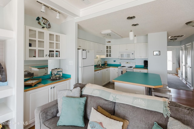 kitchen with white appliances, a sink, dark wood-type flooring, white cabinetry, and a center island