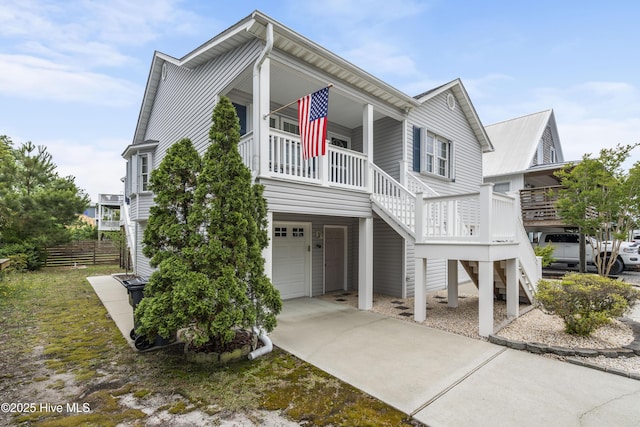 coastal home with stairs, an attached garage, concrete driveway, a porch, and fence