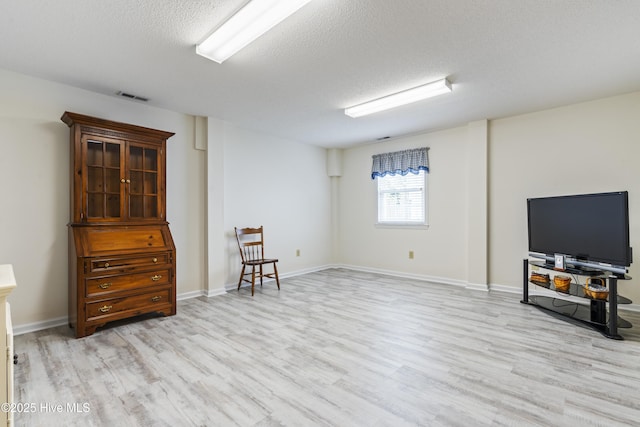 basement featuring light wood finished floors, a textured ceiling, and baseboards