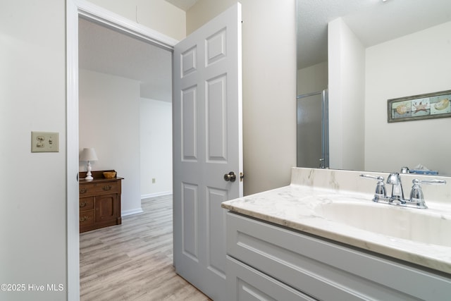 bathroom featuring vanity, wood finished floors, a shower with shower door, and baseboards
