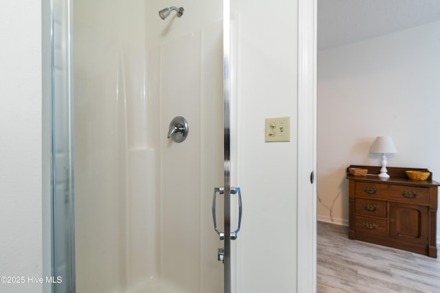 full bath with a stall shower, wood finished floors, and baseboards