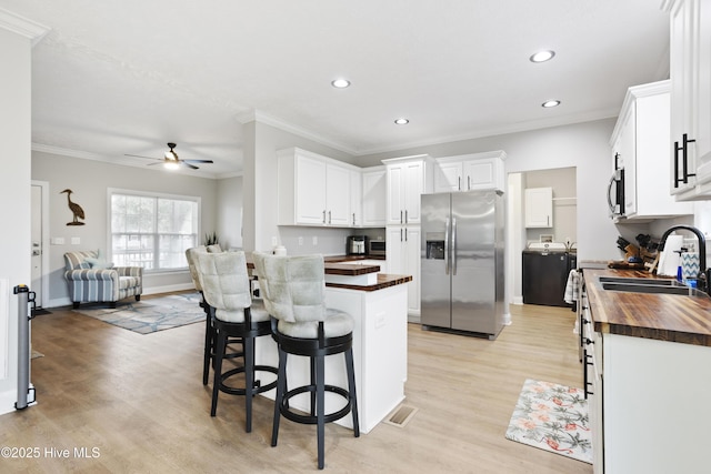 kitchen with stainless steel appliances, wood counters, crown molding, light wood-style flooring, and ceiling fan