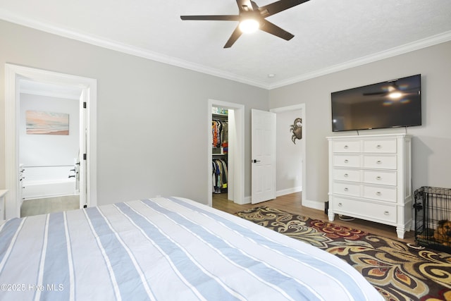 bedroom featuring wood finished floors, ornamental molding, a walk in closet, a closet, and ceiling fan