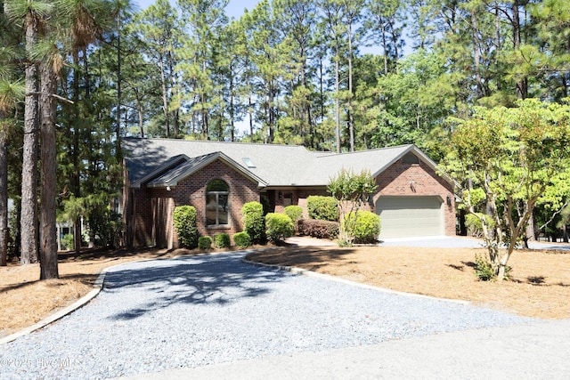 view of front of property with brick siding, gravel driveway, a garage, and view of scattered trees