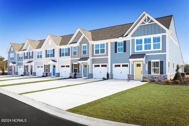 view of front facade with board and batten siding, concrete driveway, a garage, a front yard, and stone siding