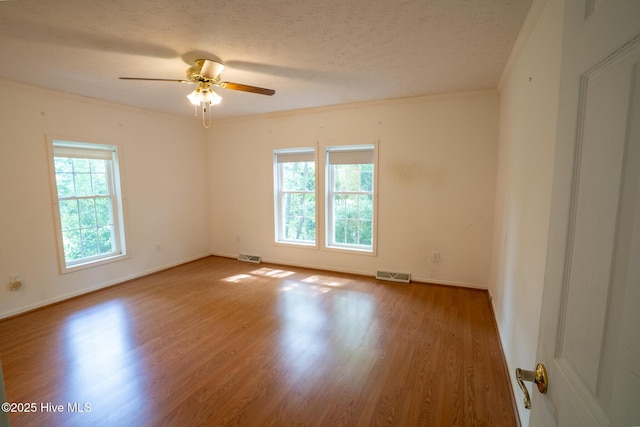 empty room featuring ornamental molding, wood finished floors, ceiling fan, a textured ceiling, and baseboards