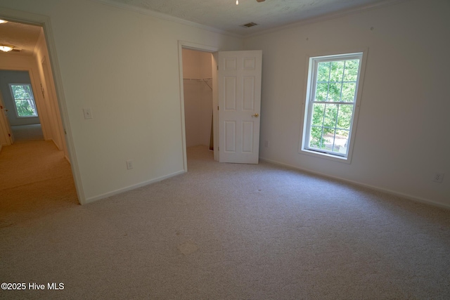 unfurnished bedroom with crown molding, light colored carpet, baseboards, a walk in closet, and a closet