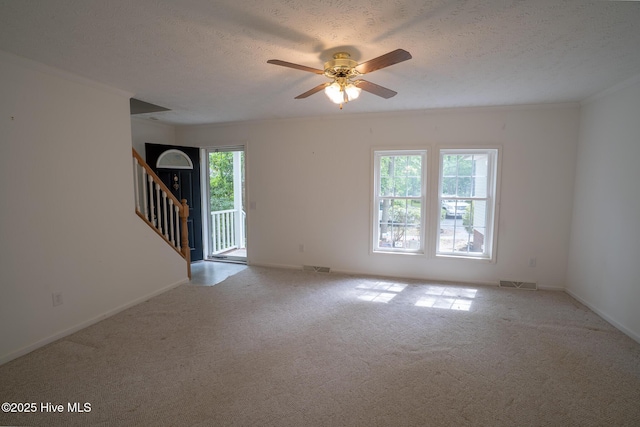 carpeted spare room with stairs, a ceiling fan, baseboards, a textured ceiling, and crown molding