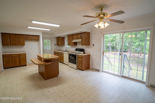 kitchen with white appliances, a sink, under cabinet range hood, light countertops, and brown cabinets