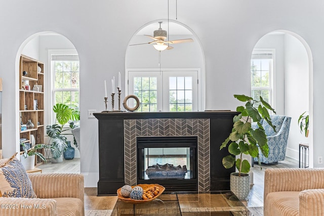living room with wood finished floors, a ceiling fan, a tiled fireplace, and arched walkways