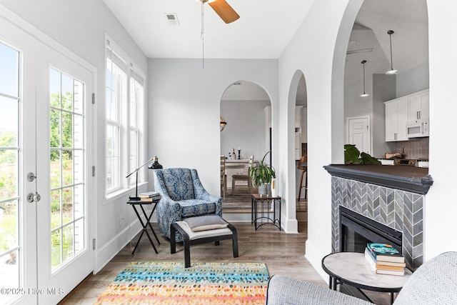 living area with healthy amount of natural light, ceiling fan, wood finished floors, and a tiled fireplace