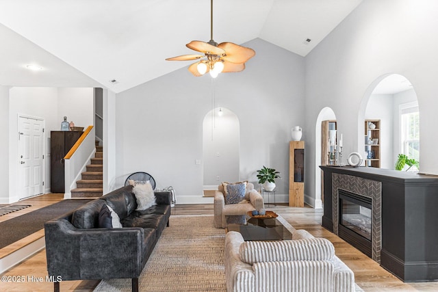 living area featuring ceiling fan, arched walkways, wood finished floors, stairs, and high vaulted ceiling