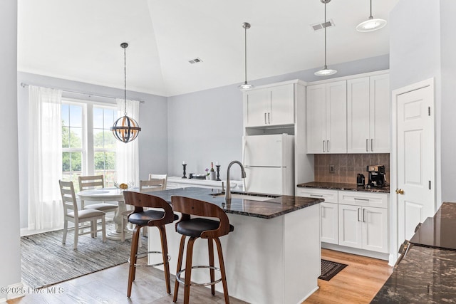kitchen featuring freestanding refrigerator, a sink, high vaulted ceiling, white cabinets, and decorative backsplash
