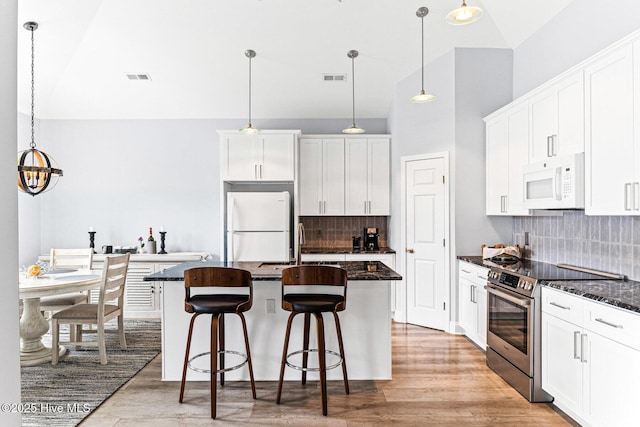 kitchen with white appliances, white cabinets, decorative backsplash, a kitchen breakfast bar, and a kitchen island