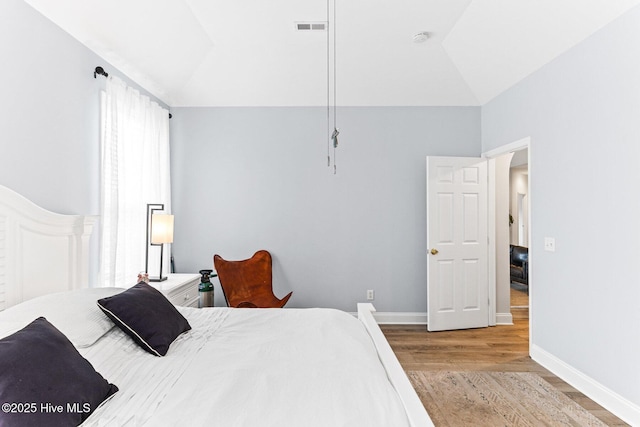 bedroom with wood finished floors, vaulted ceiling, and baseboards