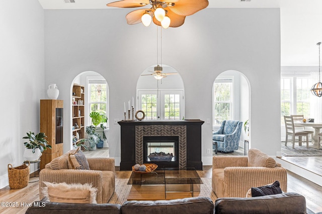 living room featuring ceiling fan, wood finished floors, a high ceiling, and a fireplace