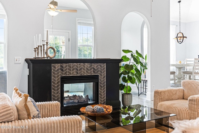 living area featuring plenty of natural light, a ceiling fan, a multi sided fireplace, and baseboards