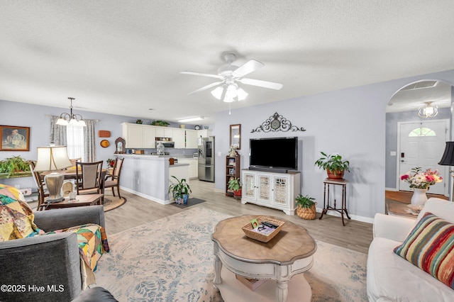 living area featuring ceiling fan, light wood-style flooring, a textured ceiling, arched walkways, and healthy amount of natural light