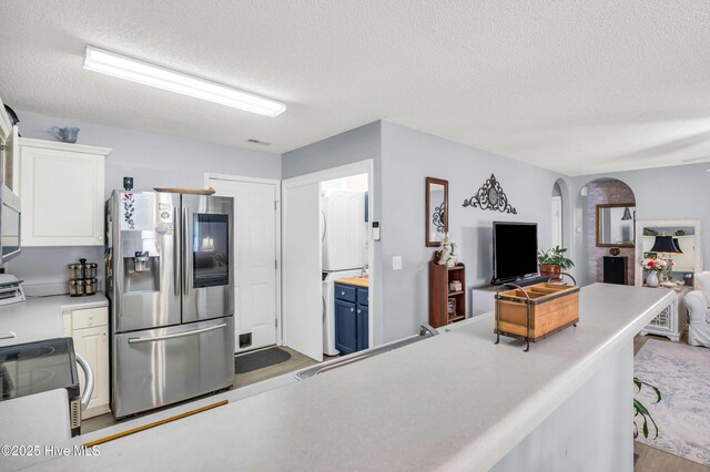 kitchen featuring stainless steel refrigerator with ice dispenser, open floor plan, a textured ceiling, light countertops, and arched walkways
