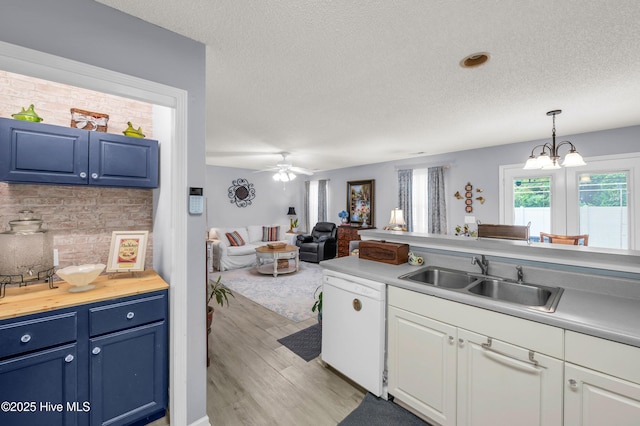 kitchen with white dishwasher, a sink, light wood finished floors, blue cabinets, and a textured ceiling
