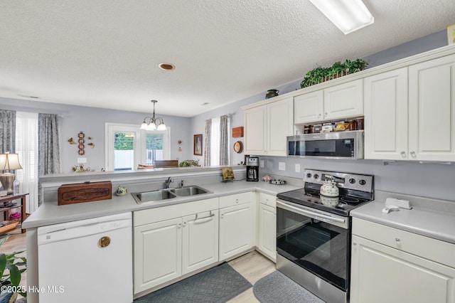kitchen featuring stainless steel appliances, a sink, a peninsula, light countertops, and a textured ceiling