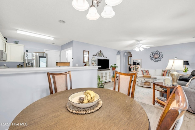 dining area with arched walkways, ceiling fan, a chandelier, and light wood finished floors