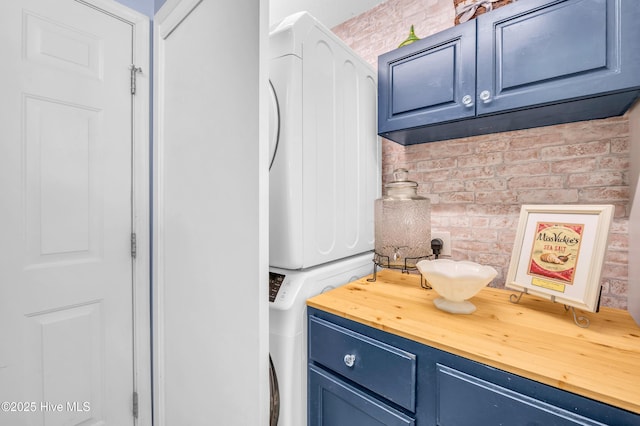 laundry room featuring stacked washer / dryer, cabinet space, and brick wall