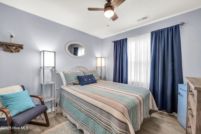bedroom with light wood-type flooring, a ceiling fan, baseboards, and a textured ceiling