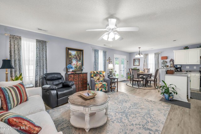 living area featuring a textured ceiling, a ceiling fan, light wood finished floors, and a chandelier