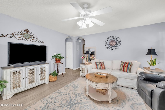 living area featuring arched walkways, wood finished floors, ceiling fan, and baseboards