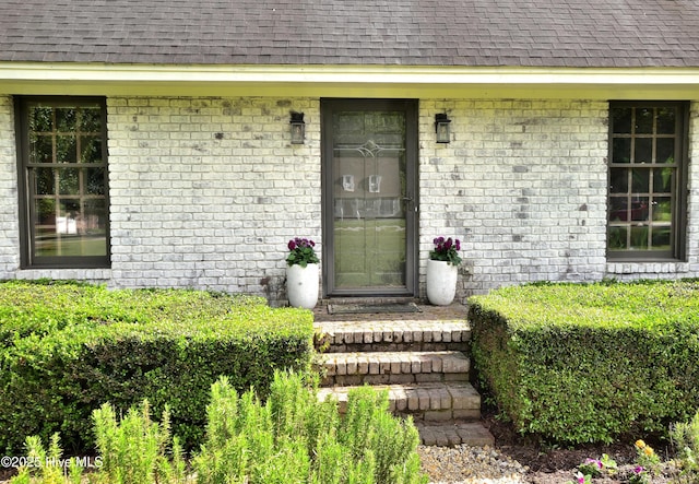 entrance to property with a shingled roof and brick siding