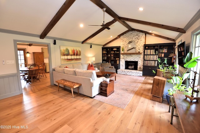 living room featuring light wood-style flooring, ceiling fan, healthy amount of natural light, a fireplace, and a wainscoted wall