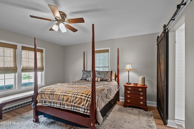 bedroom with a barn door, light wood-style flooring, multiple windows, and a baseboard heating unit