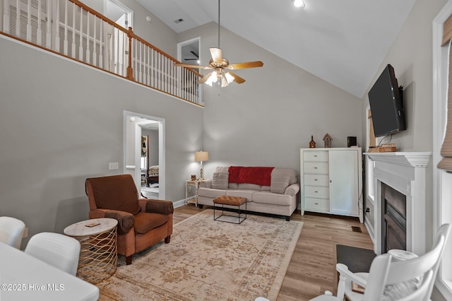 living room featuring ceiling fan, light wood-style floors, a glass covered fireplace, and high vaulted ceiling