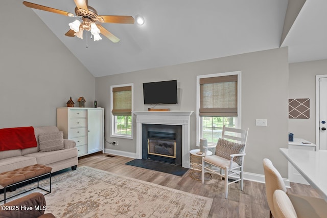 living area featuring healthy amount of natural light, vaulted ceiling, wood finished floors, and a fireplace with flush hearth