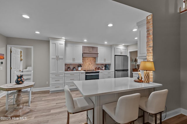kitchen with stainless steel appliances, baseboards, light wood finished floors, a breakfast bar, and recessed lighting